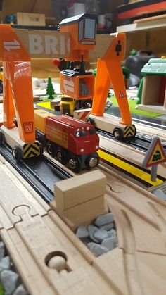 a toy train set with wooden tracks and construction vehicles on the track, in front of an orange sign that says brid