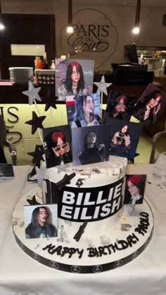 a white and black cake with photos on it sitting on a table in front of a sign