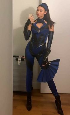 a woman in a blue outfit taking a selfie with her cell phone while wearing black gloves