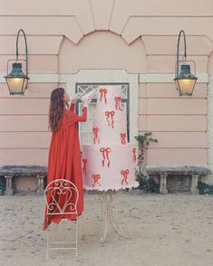 a woman standing next to a giant cake on top of a metal chair in front of a pink building