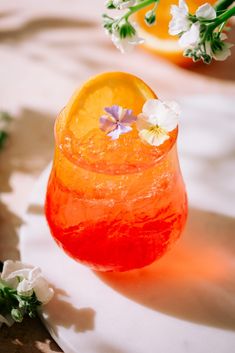 an orange and white drink with flowers on the rim, sitting on a tablecloth