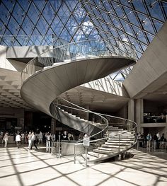 people are walking around in the lobby of a modern building with glass walls and stairs