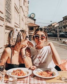 two women sitting at an outdoor table eating spaghetti