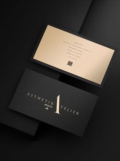 two business cards sitting on top of each other in front of a black background with gold foil