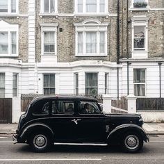 an old black car parked in front of a tall building on the side of the road