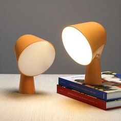 an orange table lamp sitting on top of a stack of books next to a yellow lamp