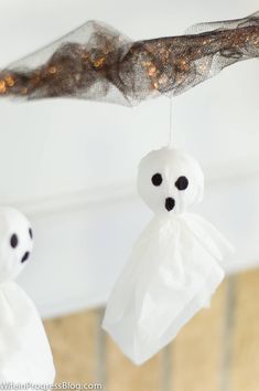 two white ghost decorations hanging from a branch