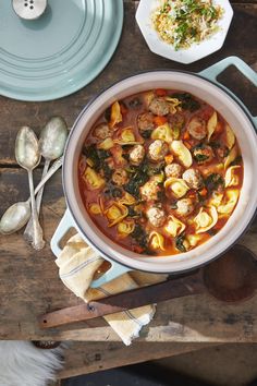 a pot filled with pasta and meatballs on top of a wooden table next to spoons