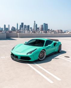 a blue sports car parked in a parking lot with the city skyline in the background