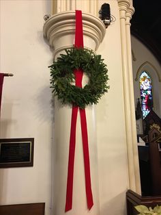 a wreath hanging on the side of a church wall with a red ribbon around it