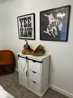 a white cabinet sitting next to a wall with pictures on it and a wooden shoe