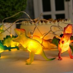 three dinosaur shaped lights sitting on top of a table next to a cake and potted plant