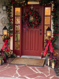 a red door decorated for christmas with wreaths and candles on the front porch,