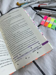 an open book sitting on top of a bed next to markers