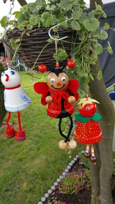 two little red and white dolls hanging from the branches of a tree in a garden