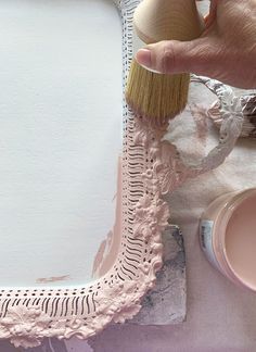 a person is painting a mirror with pink paint and a brush on the table next to it