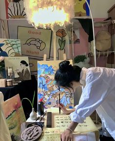 a woman working on an art project in a room filled with paintings and lights hanging from the ceiling