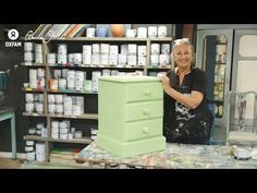 a woman is standing next to a green cabinet in a room full of paint cans