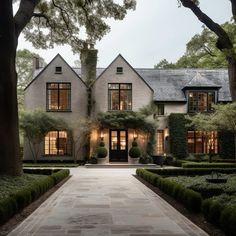 a large white house with lots of windows and bushes in front of it, surrounded by trees