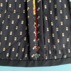 the back of a black dress with yellow and white squares on it, next to a blue background