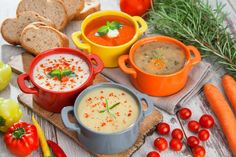 various soups, bread and vegetables on a cutting board next to each other with fresh herbs