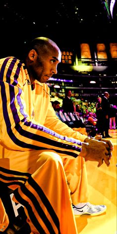 a man sitting on top of a basketball court wearing yellow and purple striped pants with his hands in his pockets