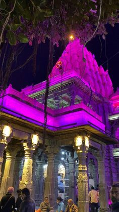 people are standing around in front of a building with purple lights on it at night