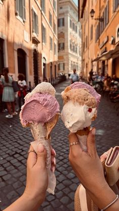 two people holding ice cream cones in their hands on a cobblestone street lined with buildings