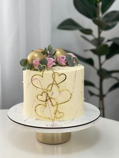 a white cake with gold decorations and pink roses