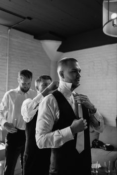 three men standing in a room with one adjusting the tie on another man's neck