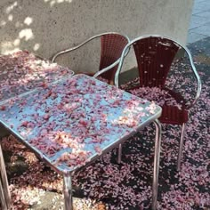 two chairs and a table covered with pink flowers on the ground next to a wall