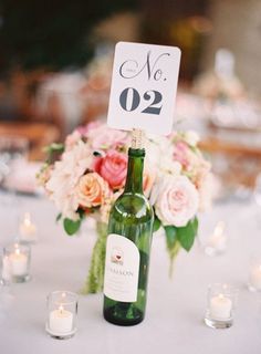 a table topped with a bottle of wine next to candles and flowers on top of a white table cloth