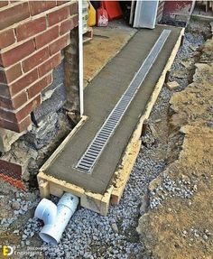 a drain pipe laying on the ground next to a brick wall and some concrete pipes