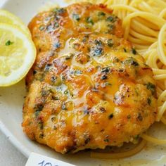 two pieces of chicken on a plate with pasta and lemon wedges