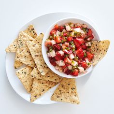 a white plate topped with tortilla chips next to a bowl filled with salsa