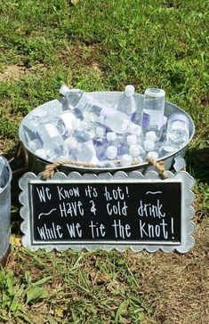 two buckets filled with ice sitting on top of a grass covered field next to a sign that says, we know it's hot have 4 cold drink while we tie the knot