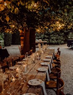 a long table set up with plates and candles for an outdoor dinner party in the evening