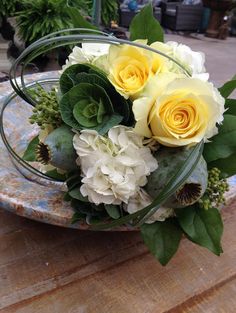 a bouquet of flowers sitting on top of a wooden table next to a vase filled with white and yellow flowers