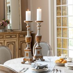 two candles sitting on top of a table with plates and silverware in front of it