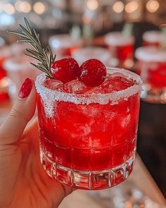 a person holding up a red drink with ice and cranberries on the rim