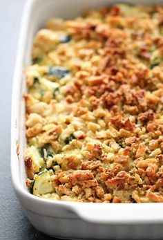 a casserole dish with zucchini and meat toppings in a white baking dish