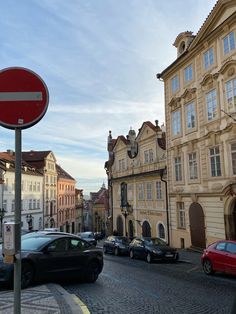 a red street sign sitting on the side of a road next to parked cars and buildings