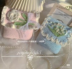 two crocheted purses sitting on top of a table next to a book