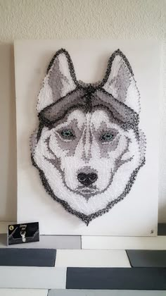 a white and gray dog with a hat on it's head is hanging on the wall