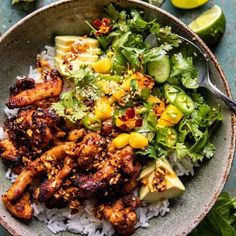 a bowl filled with chicken and rice next to lime wedges on a table top