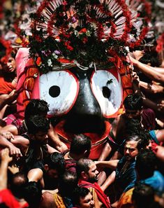 a group of people standing around a large mask with flowers on it's head