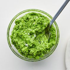 a bowl filled with green pesto next to a spoon on top of a table