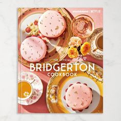 the official bridgerton cookbook on a table with plates and cups filled with food