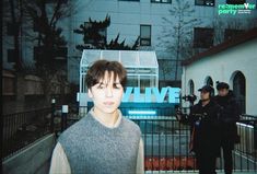 a young man standing in front of a fence with two police officers behind him on the other side