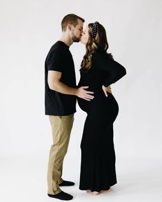 a pregnant couple kissing each other while standing in front of a white background